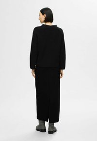 Maglione nero a coste con scollatura ampia, abbinato a una lunga gonna nera. Indossato con stivaletti alla caviglia grigi. Design semplice e testurizzato.