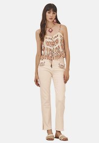 Top de tela ligera sin mangas con estampado floral y dobladillo fruncido, combinado con pantalones rosas pasteles que presentan acentos bordados en los bolsillos.