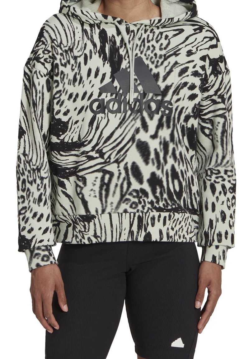 Personne portant un sweat à capuche Adidas à imprimé animal noir et blanc avec logo, associé à un short noir texturé avec un petit logo blanc.