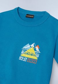 Svetta blu a collo rotondo con grafica di montagna e il testo "NAPAPIJRI geographic," "GPS-6T," e "Urban Exploration Spirit Since 1987."