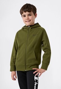 Zelená mikina na zips s hladkým povrchom, kapucňou a bočnými vreckami; má čierne logo na hrudi a manžetách, v kombinácii s čiernymi nohavicami.