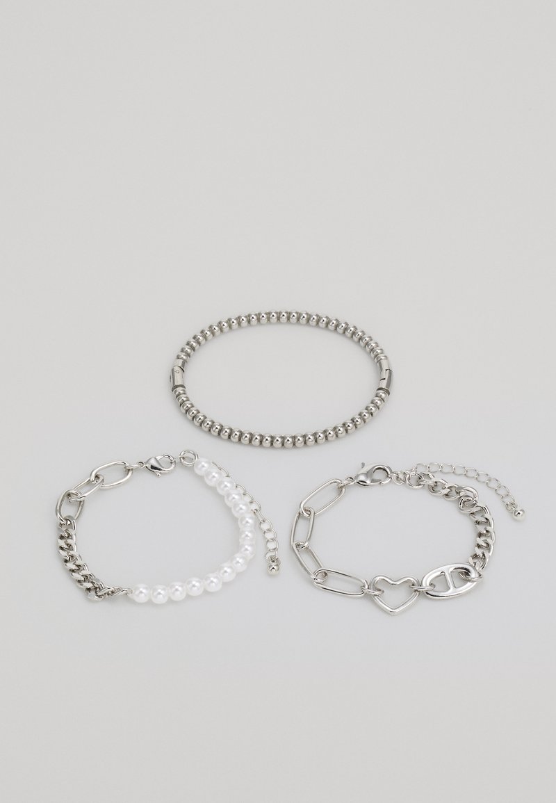 Three bracelets: a silver ball bead bracelet, a white pearl and silver link bracelet, and a silver chain bracelet with a heart accent.