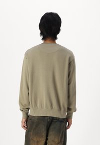 Olivengroene sweatshirt van zacht materiaal, met lange mouwen, een ronde hals en een geribbelde zoom, gedragen met donkere, vervaagde denim broek.