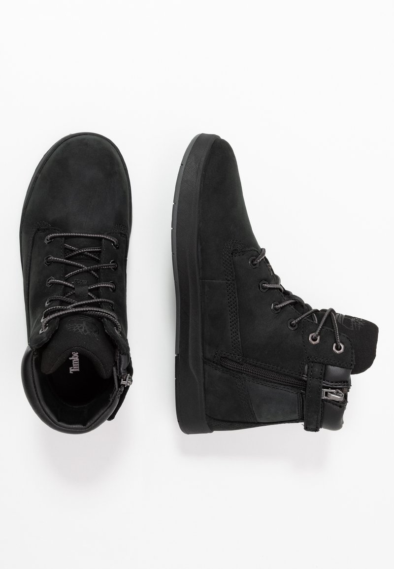 Bottines noires en daim, dotées de lacets, d'œillets en métal et d'une fermeture éclair sur le côté. La semelle est en caoutchouc avec un motif de grip texturé.