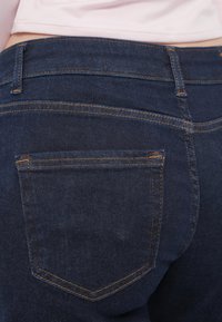 Μπλε τζιν με κλασικό σχέδιο, διακοσμημένο με πορτοκαλί ραφές, πίσω τσέπες και λεία υφή.