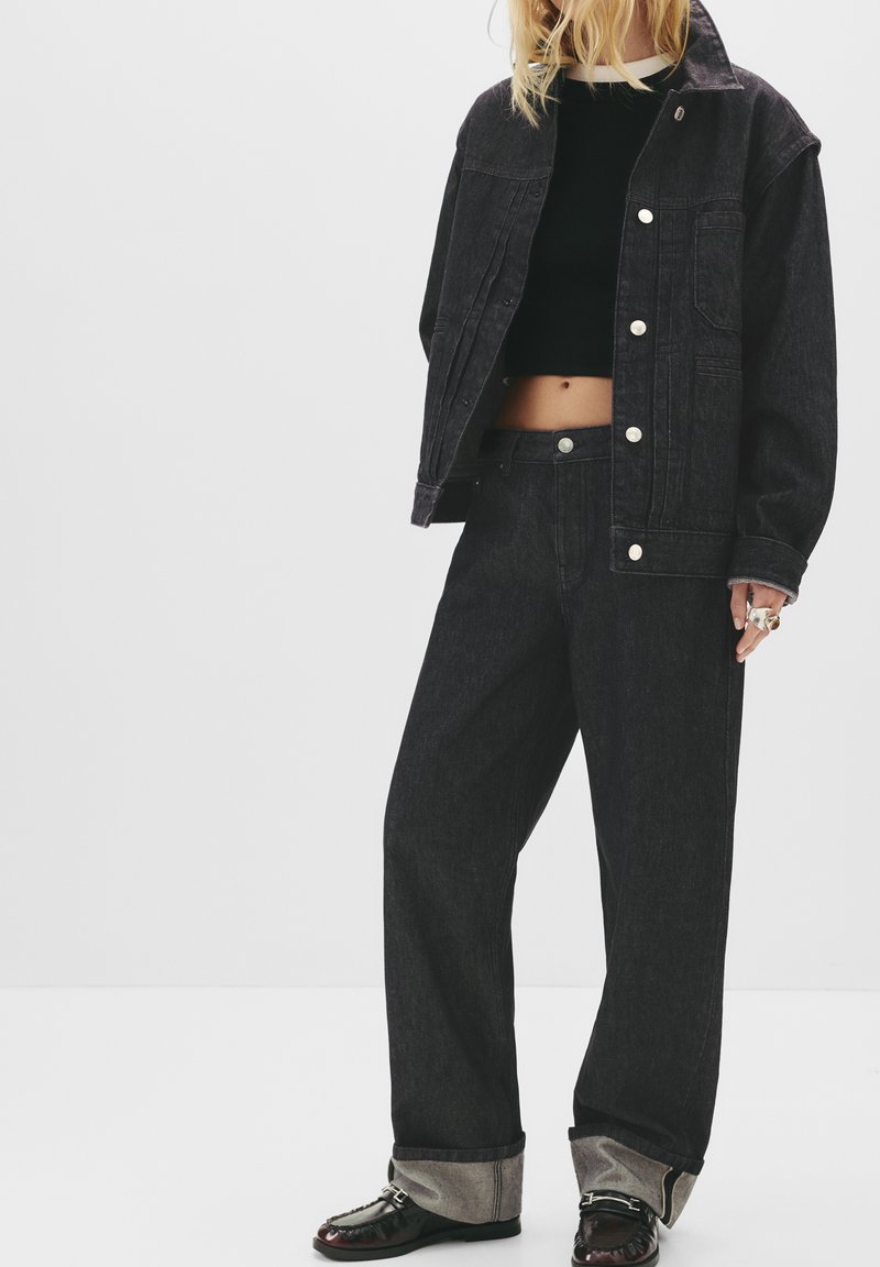 Zwarte denimjas en wijde jeans. De jas heeft een cropped fit, knoopsluitingen en voorzakken. De jeans hebben opgerolde mouwen en een ontspannen silhouet.