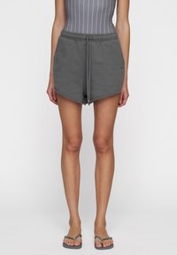 Pantalones cortos de mezcla de algodón grises con cintura ajustable, presentan un dobladillo deshilachado y una forma relajada. Combinados con chanclas grises.