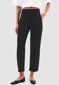 Hoge taille zwarte broek met een gladde textuur, een op maat gemaakte pasvorm, zijzakken en een recht gesneden ontwerp. Gecombineerd met platte zwarte schoenen.