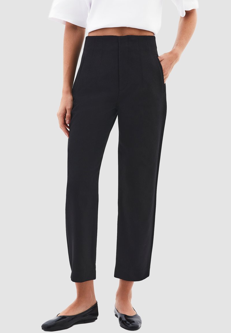 Hoge taille zwarte broek met een gladde textuur, een op maat gemaakte pasvorm, zijzakken en een recht gesneden ontwerp. Gecombineerd met platte zwarte schoenen.