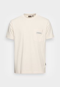 Camiseta de algodón color beige claro con cuello redondo, mangas cortas y un bolsillo en el pecho que cuenta con una etiqueta de tela de la marca. Corte simple y recto.