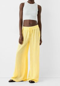 Ribbade vita crop-toppar kombinerat med vida, lätta gula byxor med vertikala randiga mönster och en justerbar dragsko i midjan.