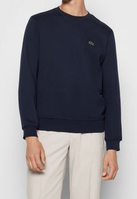 Námořnický crewneck svetr vyrobený z texturované bavlny. Obsahuje lemy na rukávech a spodním okraji, s malým zeleným logem na hrudi.