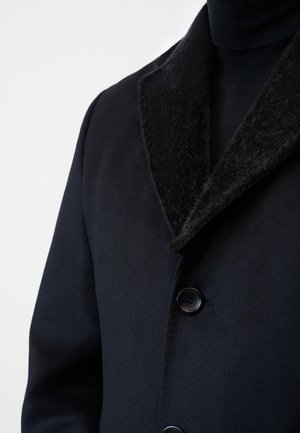 Cappotto nero con un colletto in pelliccia nera testurizzata, design a un solo petto e due bottoni. Il tessuto appare liscio e morbido.