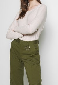 Beige långärmad tröja gjord av mjukt tyg, ihop med gröna cargobyxor med en silverring som accent vid midjan och sidofickor.