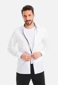 White button-up shirt with a contrasting navy trim along the collar and button placket, featuring long sleeves and a tailored fit.
