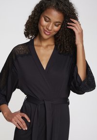 Must muströöp, mis on valmistatud pehmest kangast, millel on pitsaktsendid varrukatel ja seotud vöö puusal.