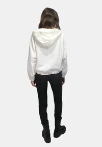 Giacca bianca con cappuccio, con vita cintrata e polsini elastici, abbinata a jeans neri aderenti e stivali neri chunky.