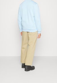 Felpa azzurra chiara con orli e polsini a costine, abbinata a pantaloni beige a gamba larga e stivali neri alla caviglia.