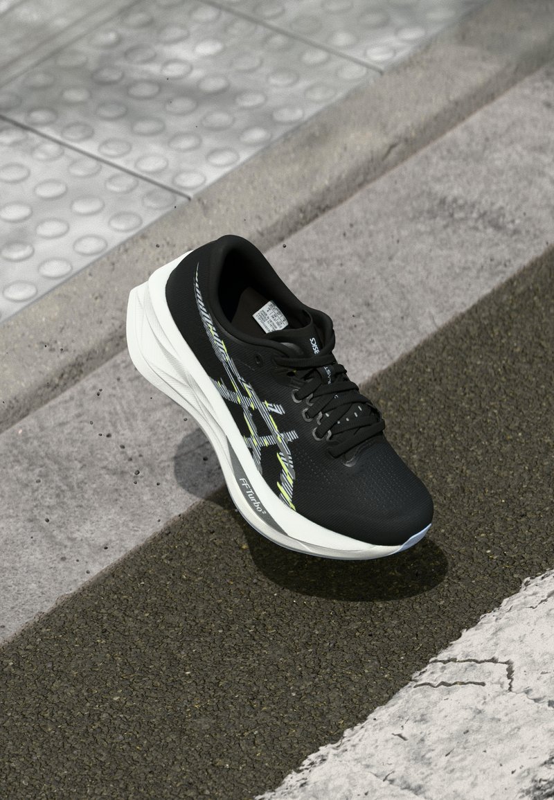 Chaussure de course noire avec une tige en maille texturée, des accents réfléchissants en jaune et blanc, et un design de semelle blanche rembourrée.
