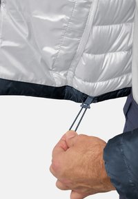 Leichte silberne Pufferjacke mit navyfarbigem Saum, ausgestattet mit einem Kordelzugverschluss. Eine Hand hält den Kordelzug zur Anpassung.