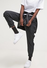 Black athletic joggers with a tapered fit and zippered cuffs, paired with a white t-shirt and white sneakers. Smooth, lightweight material.