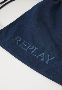 Námořnická džínsová taška na stahovací šňůrku s vyšívaným logem "REPLAY", která předvádí texturovanou látku a ležérní design.