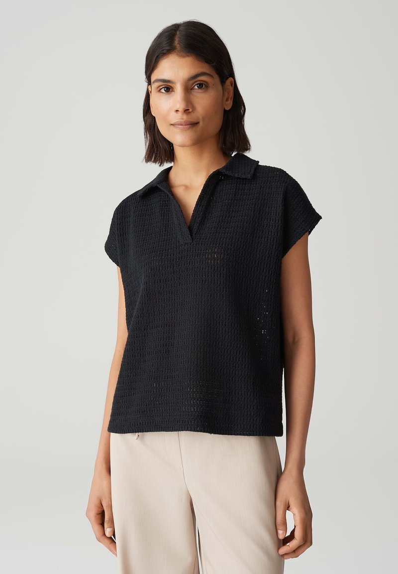 Polo nero a maniche corte realizzato in tessuto strutturato, con colletto a v e vestibilità ampia. Design semplice senza motivi o accenti visibili.