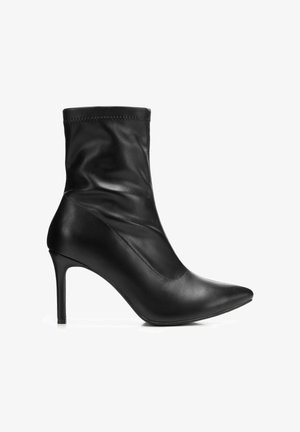 Bottine en cuir noir à bout pointu et talon aiguille fin, tige souple froncée, vue de côté sur fond blanc.
