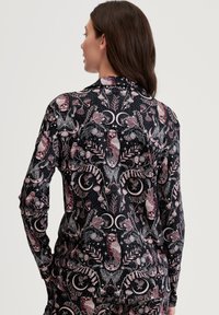 Langarmshirt met een zwarte basis, versierd met een gedetailleerd patroon van een uil en bloemen in tinten van roze en crème. Glad stoffen textuur.