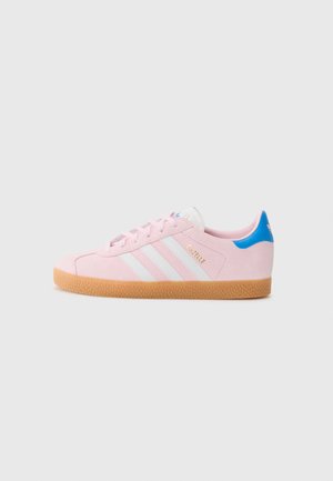 Light pink suede sneakers with white stripes and gold text. Features a blue accent on the heel and a textured gum sole.