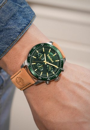 Zielony zegarek chronograficzny z fakturowanym brązowym skórzanym paskiem, metalicznymi akcentami i czarną tarczą z złotymi znacznikami godzin i sub-tarczami.