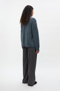 Maglione blu oversize e testurizzato con maniche lunghe, abbinato a pantaloni a righe sottili neri a vita alta, visto da dietro.