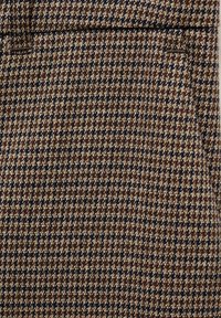Hnědý houndstooth látka s krémovými a námořnickými akcenty, s texturovaným povrchem a tradičním čtvercovým vzorem.