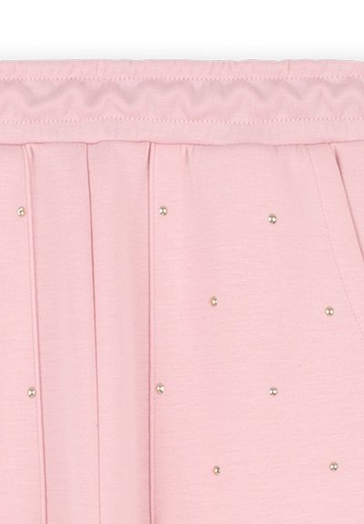 Tissu plissé rose clair avec une taille smockée, rehaussé de petites rivets dorés espacés de manière égale sur la surface.