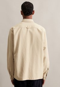 Beige getextureerde shirt met een kraag, knoopmanchetten en een rugpaneel, voorzien van een subtiel patroon en een relaxed pasvorm.