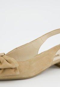 Béžová semišová balerína na nízkém podpatku se zavazováním za patu a velkou dekorativní mašlí na přední straně.