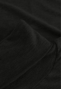 Melnā audumā ar gludu tekstūru, redzamas krokas un drapējums. Materiāls izskatās viegls un mīksts, uzsverot tā smalko, vienmērīgo adījumu.