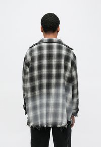 Μαύρο και γκρι πουκάμισο φανέλας με καρό σχέδιο, ξεφτισμένο τελείωμα, ριχτούς ώμους και γιακά, με υφή στο ύφασμα και χαλαρή εφαρμογή.