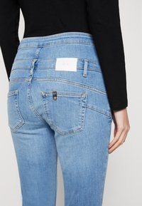 Jeans de mezclilla azul claro con un diseño ajustado. Cuentan con una cintura alta, dos bolsillos traseros y una etiqueta de marca blanca en la cinturilla.