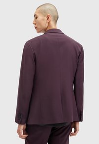 Blazer violet foncé au design élégant, coupe ajustée, revers crantés et boutons décoratifs aux poignets. Texture de tissu lisse.