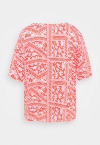Blouse corail à manches courtes avec motifs floraux blancs et carrés géométriques dans le dos, avec une coupe ample et carrée.