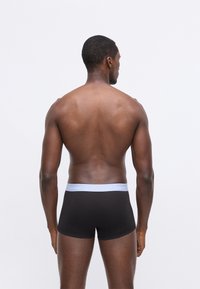 Fekete boxer alsónadrág fehér Calvin Klein logós derékszíjjal, hátulról bemutatva, kiemelve az sima anyagot és a testhezálló fazont.