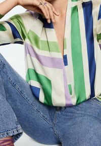 Blusa a fantasia geometrica con strisce verdi, blu e viola; realizzata in tessuto leggero, presenta un profondo scollo a V e una vestibilità morbida.