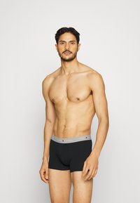 Schwarze Boxershorts aus weichem Material mit einem grauen elastischen Bund, der das Tommy Hilfiger-Logo trägt, und einer enganliegenden Passform.