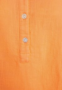 Chemise en lin orange avec une finition texturée, dotée d'une patte de boutonnage et de trois boutons ronds de couleur claire le long de la patte.