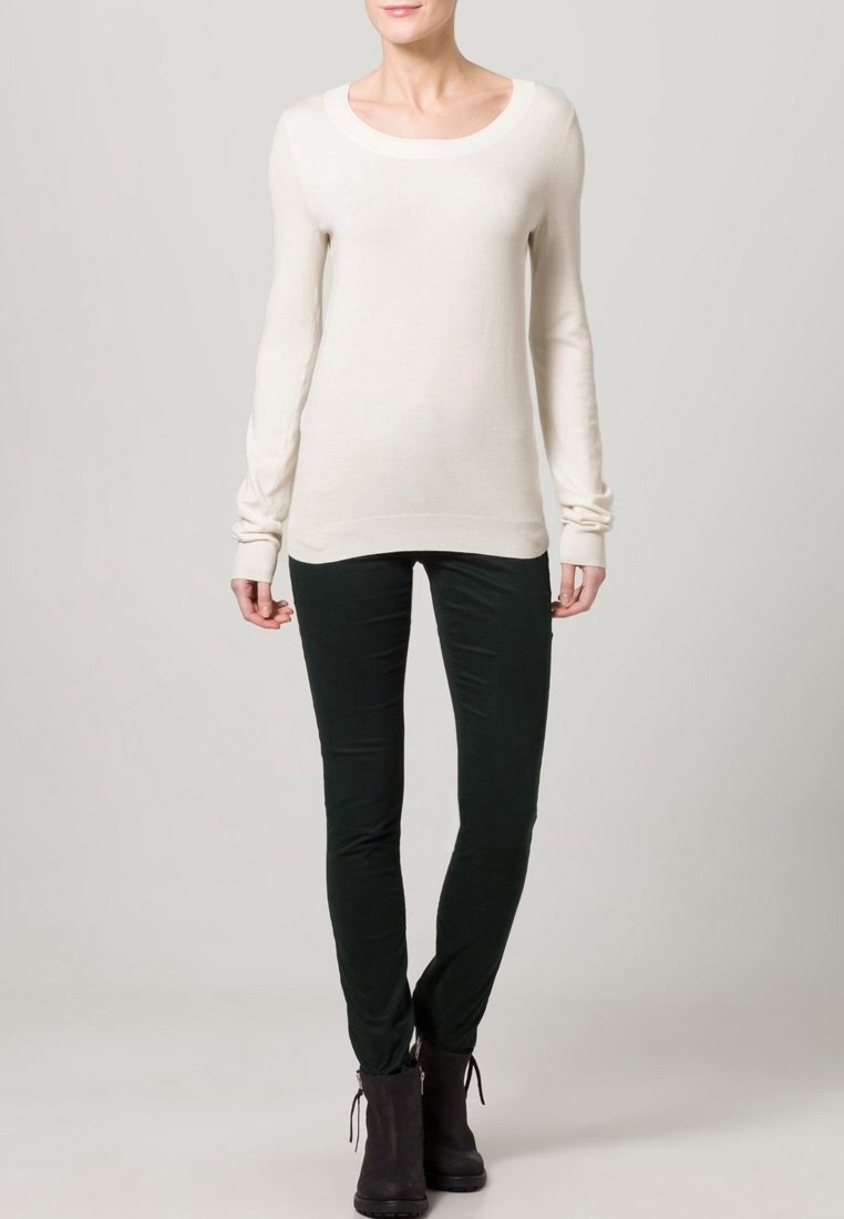 Maglione beige chiaro a maniche lunghe con scollo a barchetta, abbinato a pantaloni fitted verde scuro e stivaletti neri. Tessuto morbido e testurizzato.