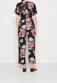 Mono floral negro de manga corta, con patrones de flores rosas y blancas, cintura ajustada con cinturón y piernas anchas. Textura de satén suave.