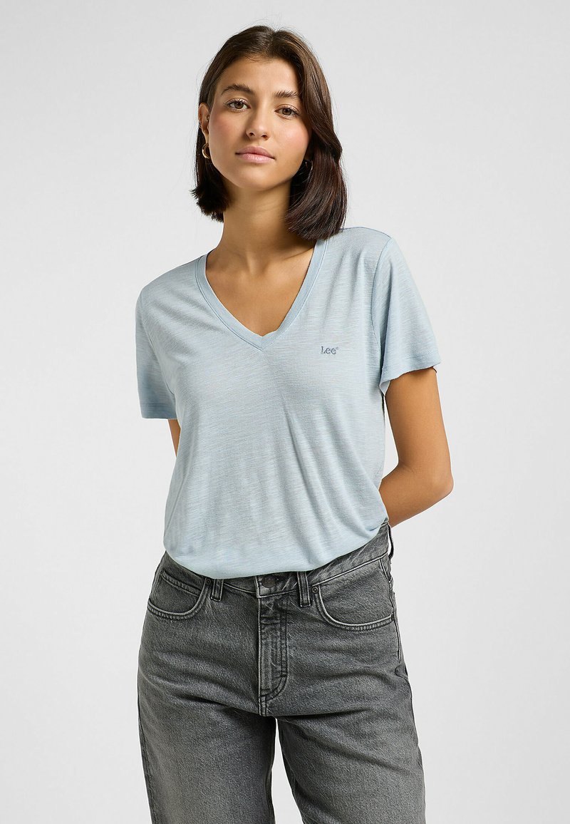 T-shirt azzurro chiaro a scollo a V in morbido tessuto, maniche corte, con un piccolo logo ricamato, abbinato a jeans a vita alta grigi scuri.