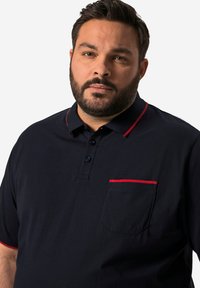 Námořnické polo tričko s červeným límečkem a akcentem kapsy; vyrobené z jednobarevné látky, s třemi knoflíky na přední straně.