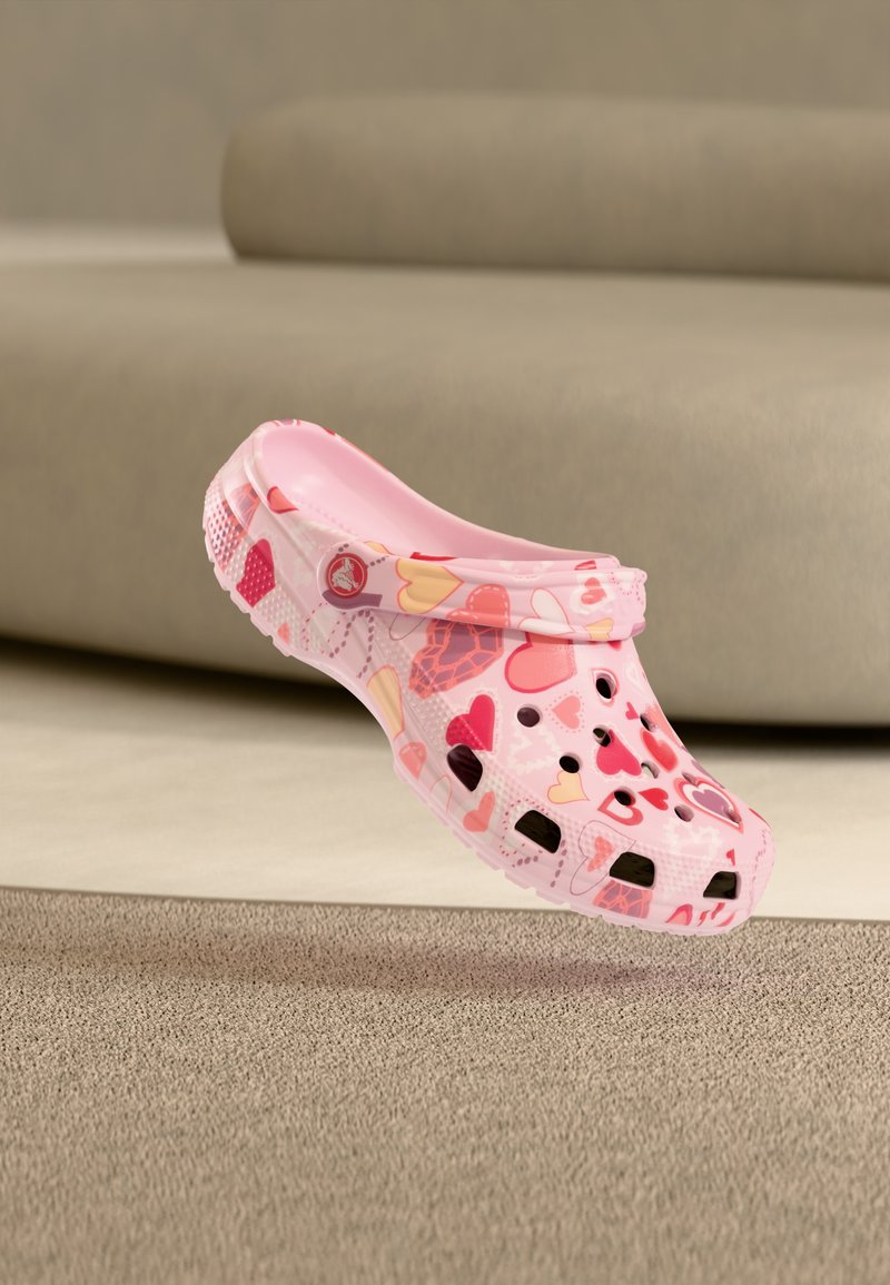 Rosa Clogs mit Herzmustern, hergestellt aus leichtem Material, mit Belüftungslöchern, einem Rückriemen und einer strukturierten Sohle für besseren Halt.
